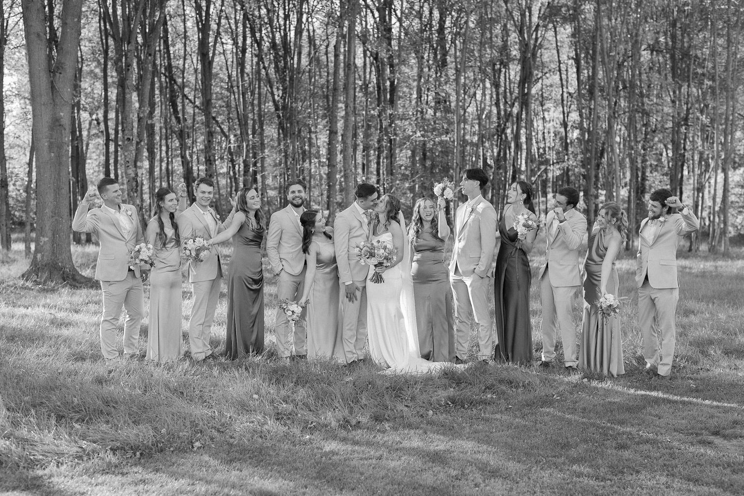 Wedding party gathered in a wooded outdoor setting for group photos.