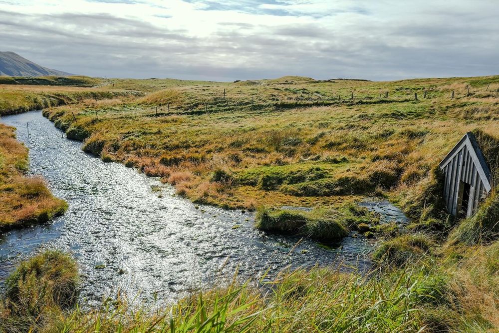 Rocky stream flows through green Icelandic landscape with mountains in background.