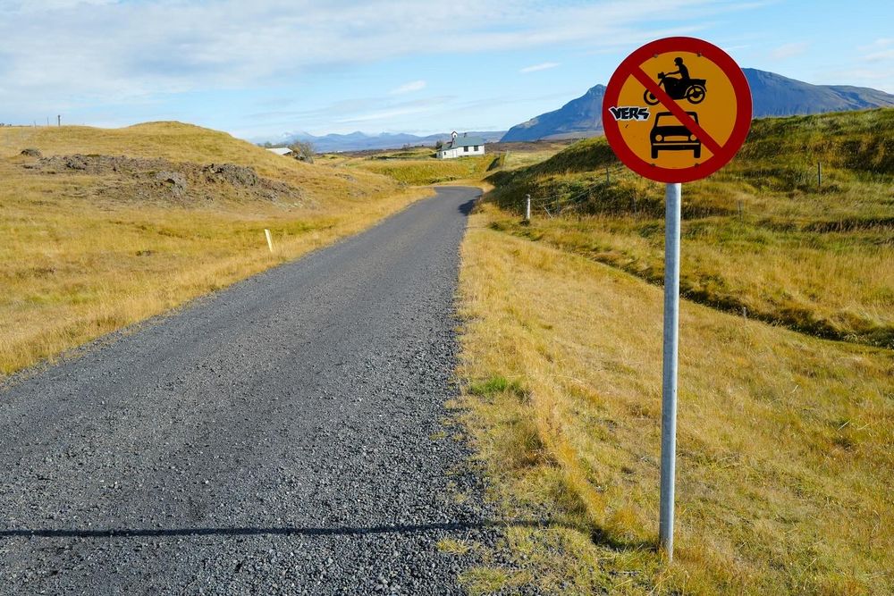 Rural gravel road in Iceland with no-entry traffic sign against mountainous backdrop.