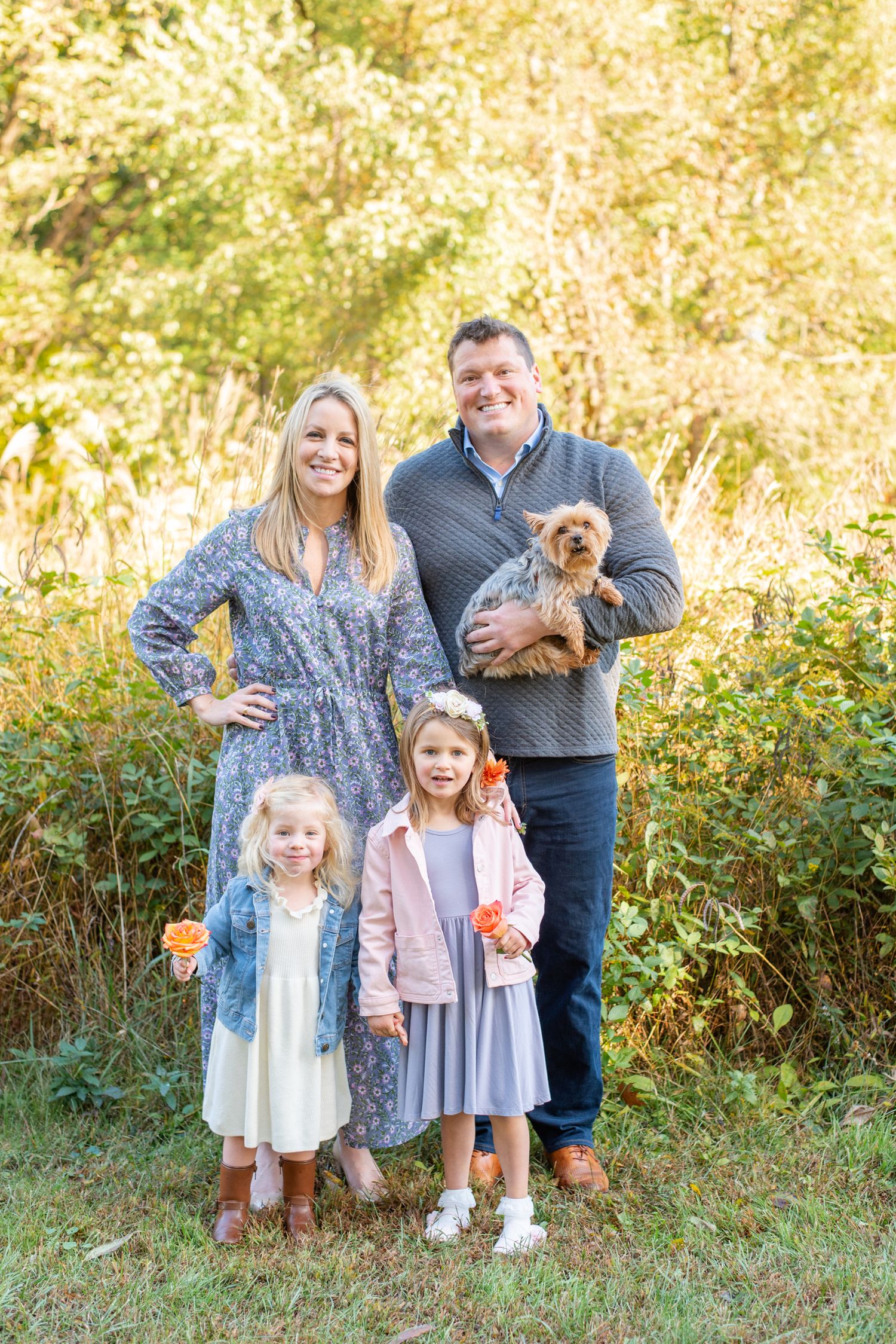 Beautiful autumn outdoor family portrait with small brown dog and glowing golden foliage background in Arlington, VA park