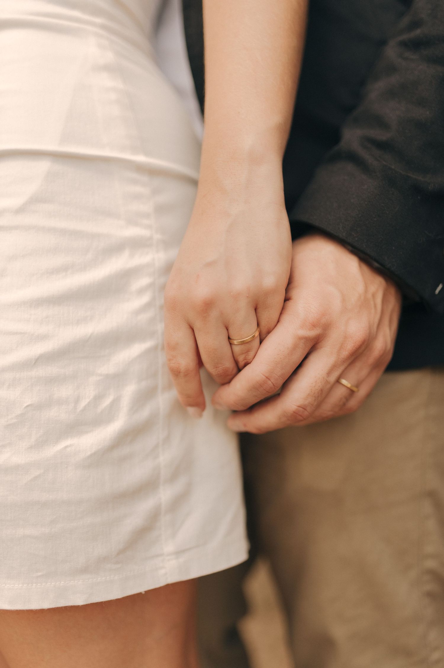 Close-up of couple's hands with wedding rings against white and black formal attire.