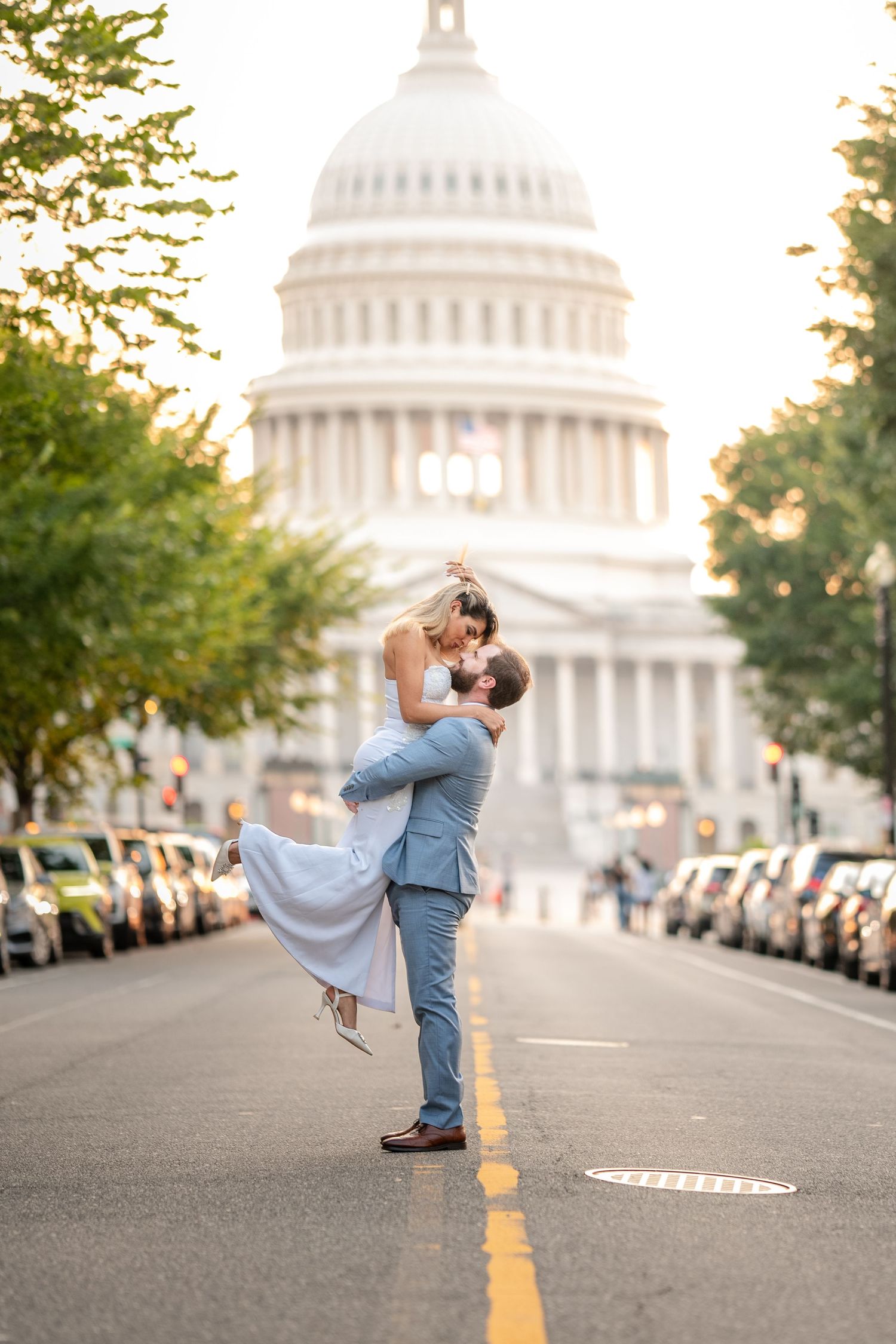 Romantic couple shares a joyful embrace in the middle of a city street, with the U.S. Capitol building beautifully framed in the background.