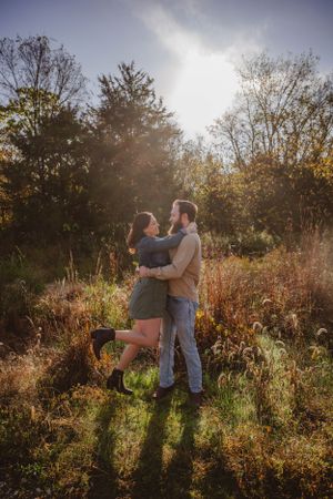Couple sharing an intimate embrace in autumn sunlight surrounded by trees and tall grass.