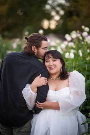 Couple in formal attire sharing a tender moment in a garden with blooming flowers.