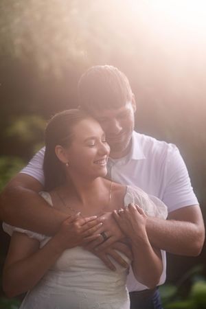 A romantic outdoor photoshoot showing a couple embracing and laughing together in soft sunlit lighting.