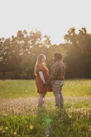A romantic sunset moment captured in a grassy field with golden light filtering through trees in the background.