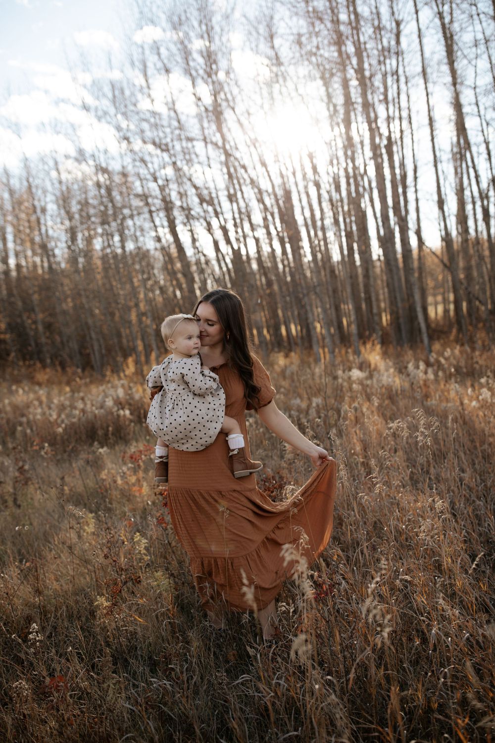 Joyful moments shared in a sunlit field surrounded by tall autumn grasses and bare trees.