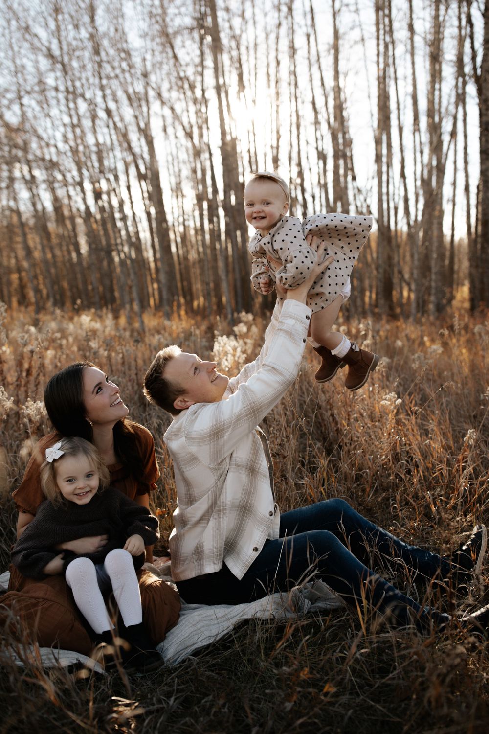 Playful family interactions captured against a backdrop of bare trees and tall grass.