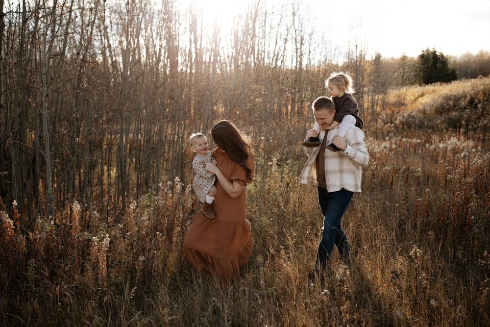 Candid family photography in an autumn field with bare trees at sunset.