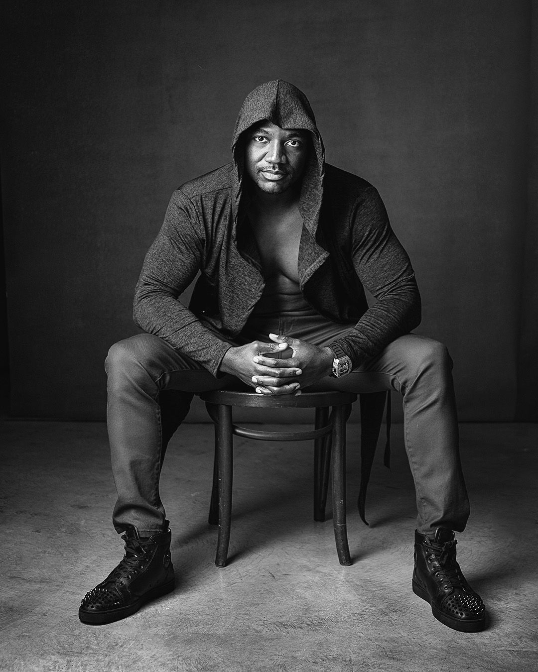 Dramatic black and white portrait of a person in a hoodie seated on a chair.