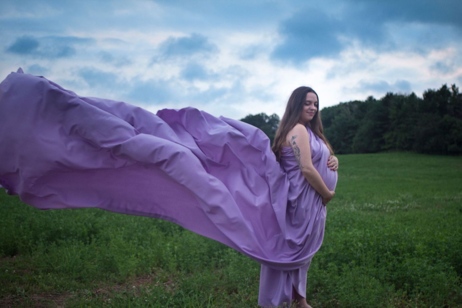 Image of a woman holding her baby bump with purple fabric blowing in the wind.