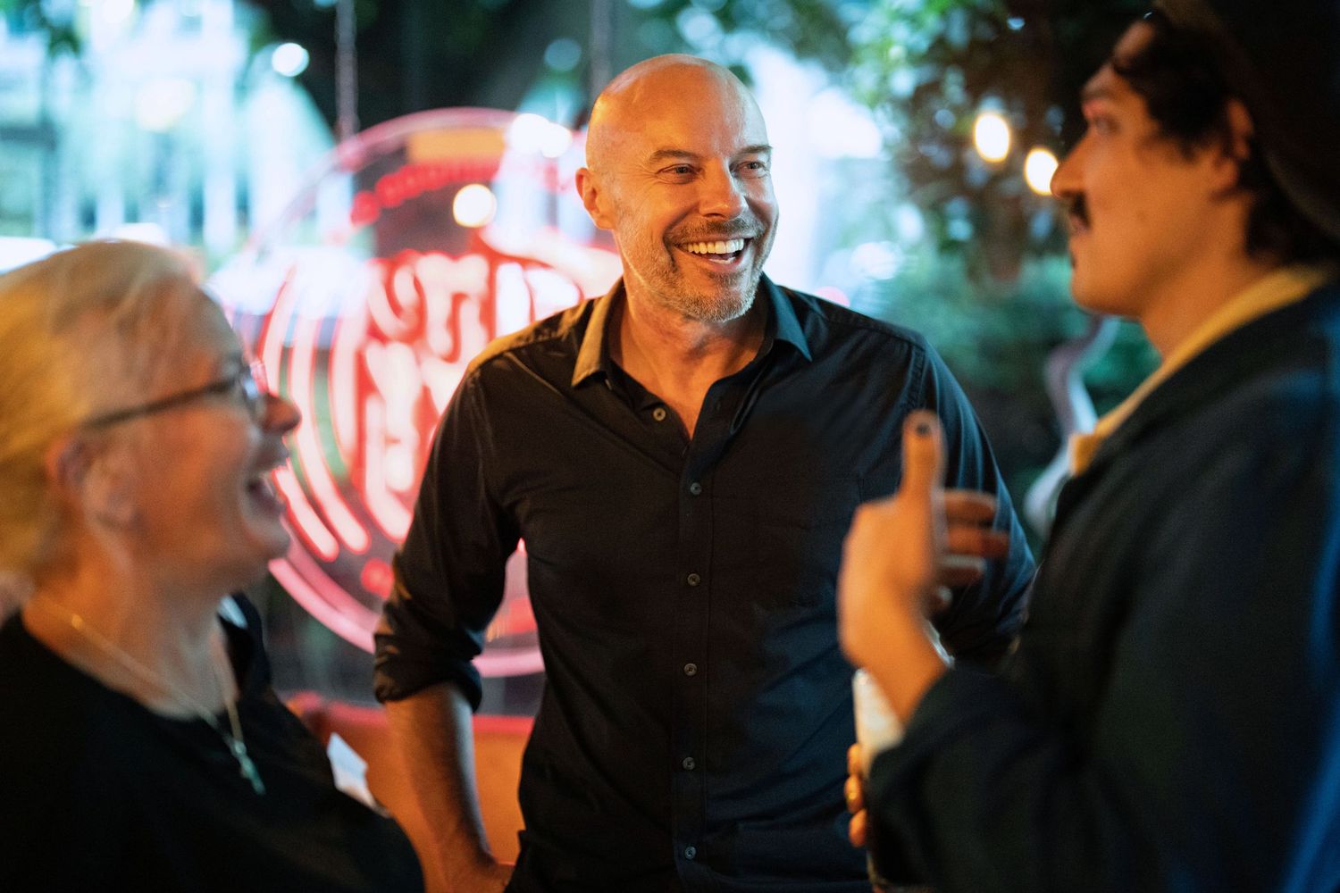 Photographer Gary Williams in a lively nighttime conversation between people with neon lights glowing in the background.