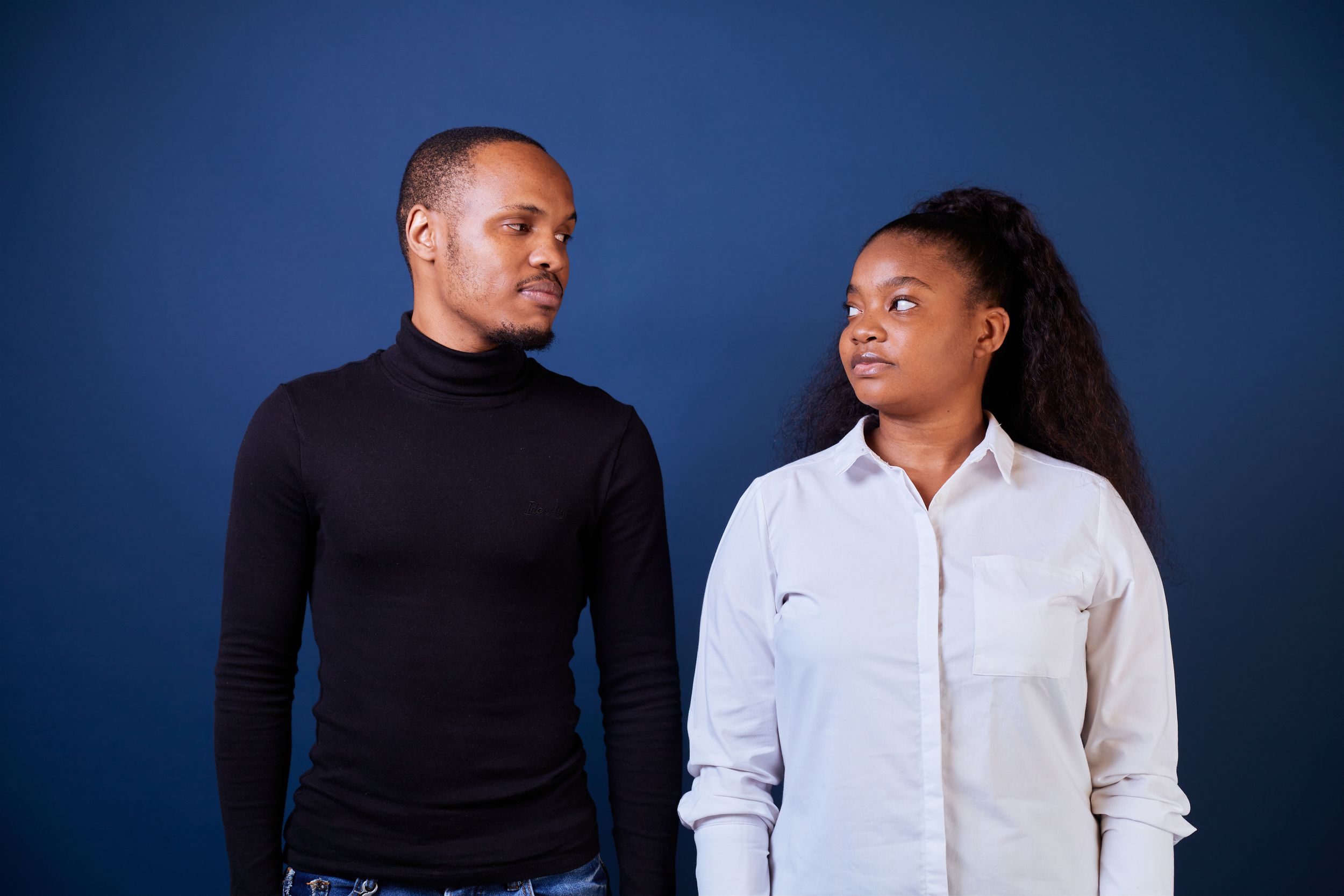 Two people in formal attire pose for a professional photo shoot against a dark blue background.