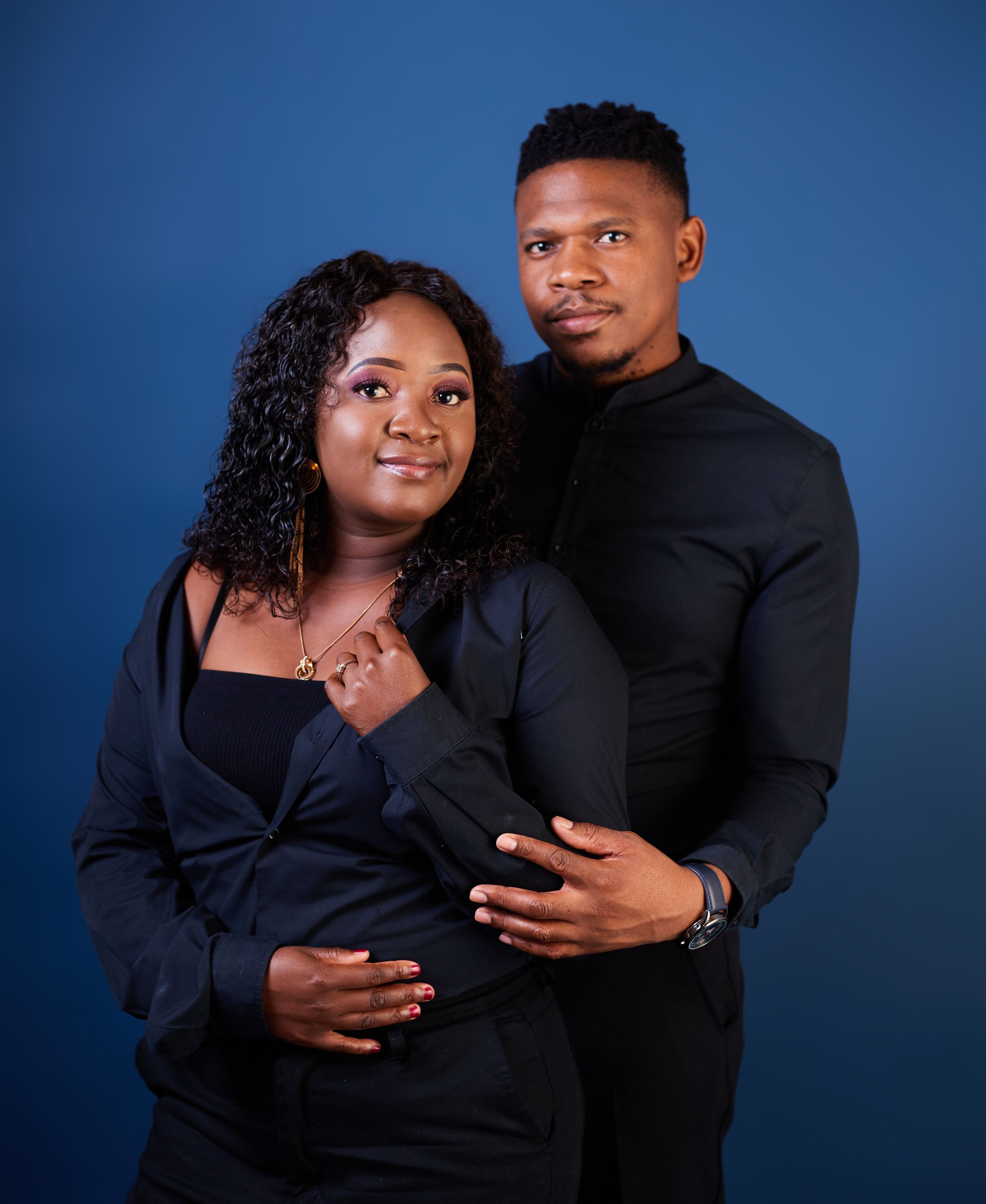 A couple in matching black outfits embrace during a romantic photo session.