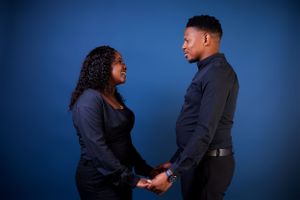 Two people share an intimate moment during a professional photo shoot with blue lighting.