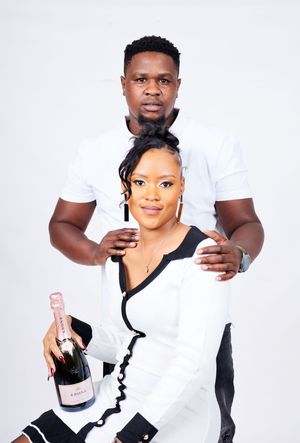 A couple in black and white outfits poses with champagne during a celebratory studio session.