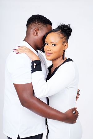 A romantic studio portrait of a couple embracing in matching white outfits.