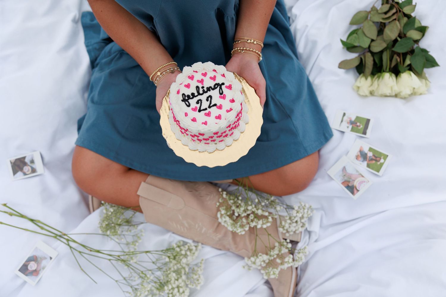 White birthday cake decorated with pink hearts photographed from above with flowers.