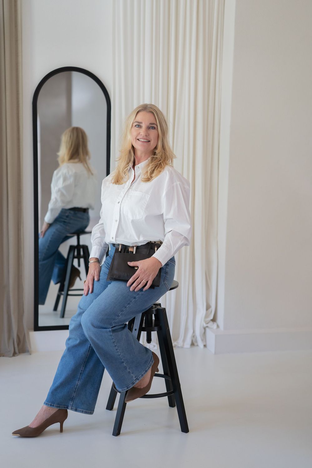 Fashion model in white blouse and jeans poses on black chair against white backdrop in studio photo collage.