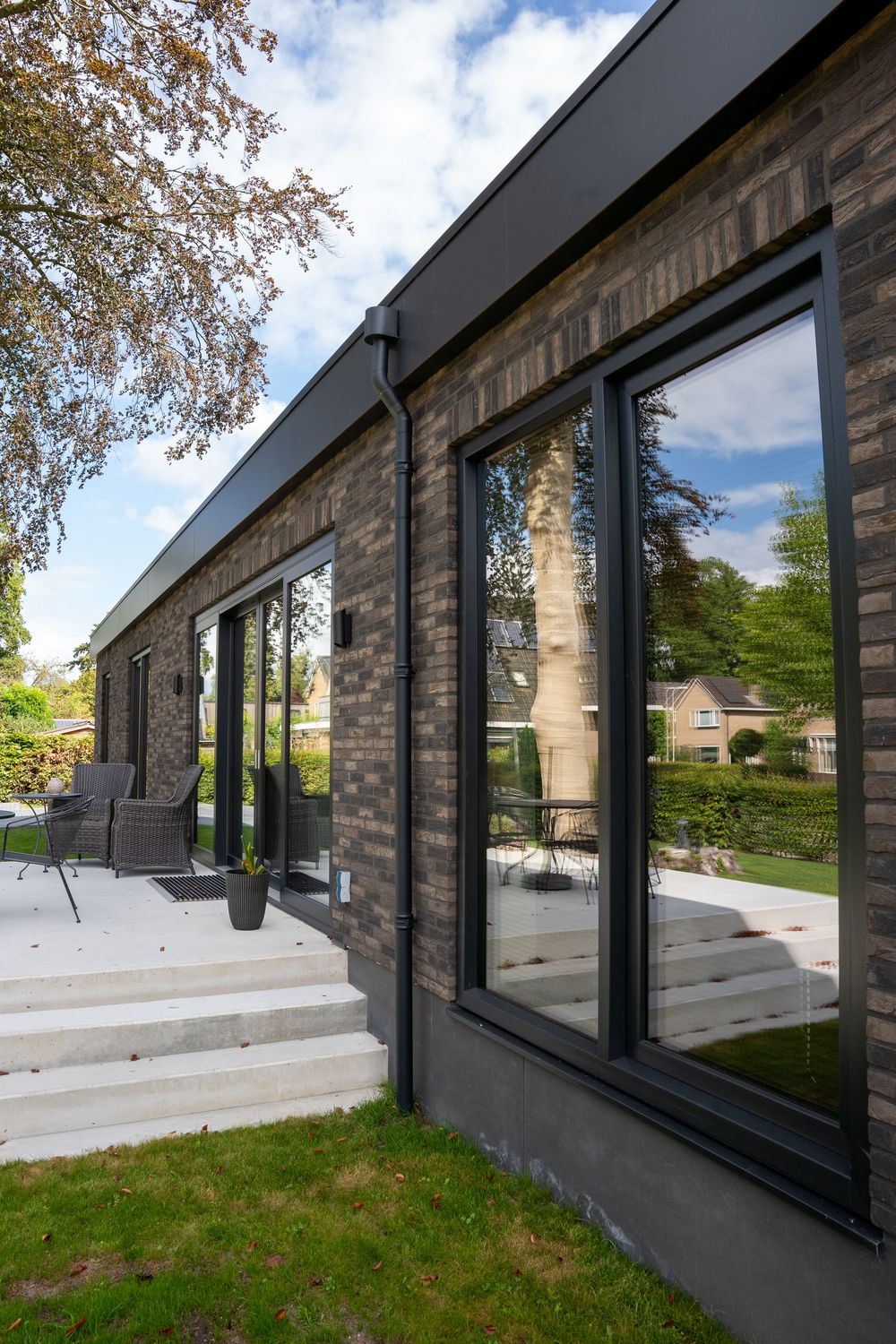 Modern black-framed windows wrap around a corner of a brick building with a concrete foundation and overhanging eaves.