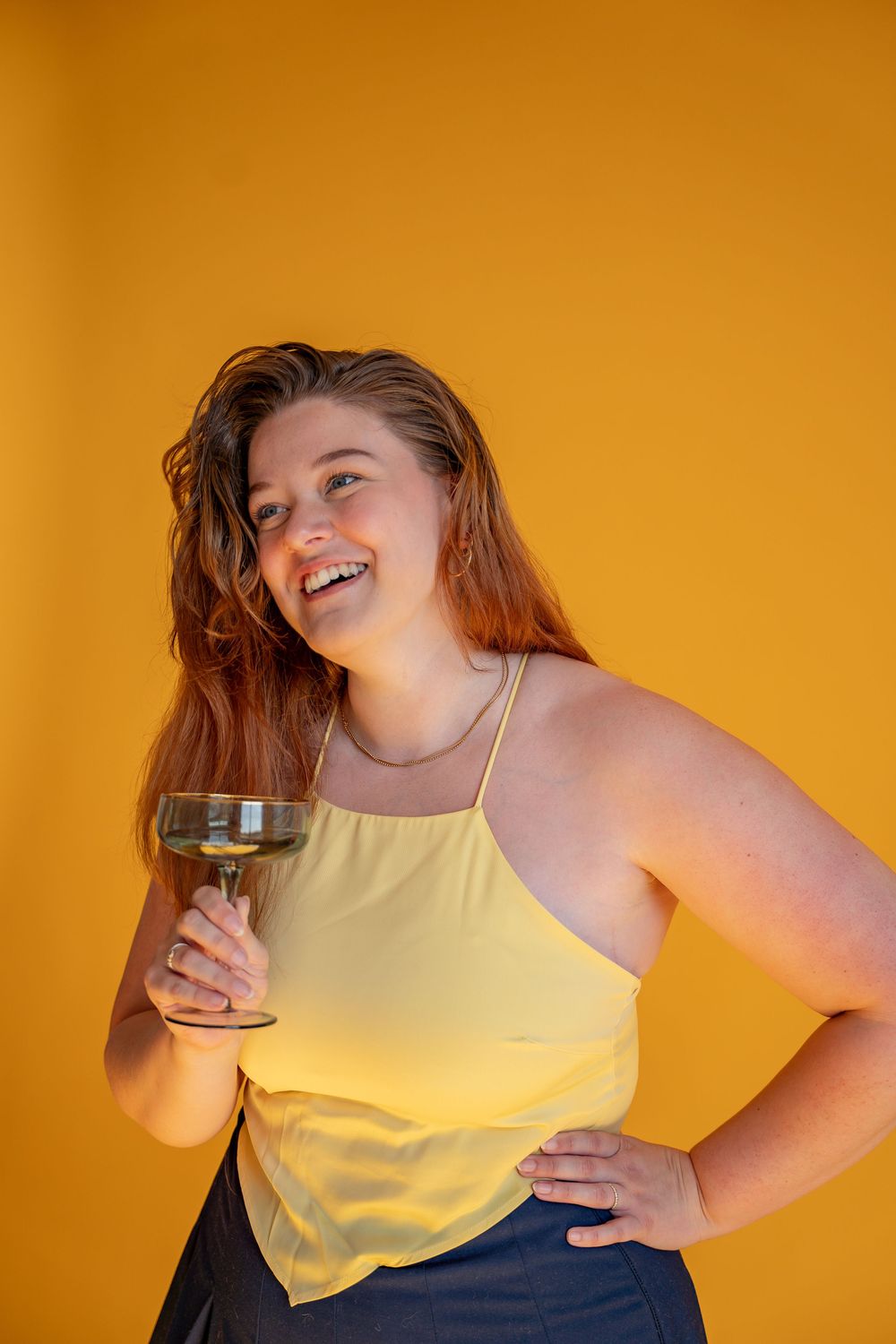 A series of photos showing someone in a yellow tank top against an orange background posing with a drink.