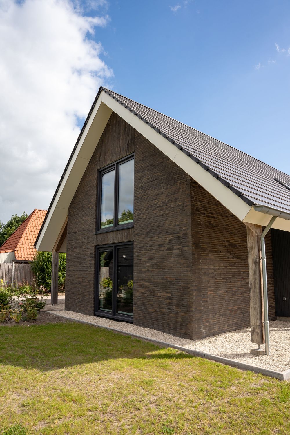 Modern house exterior with angled roof features brown stone facade and large windows set against grassy landscape.