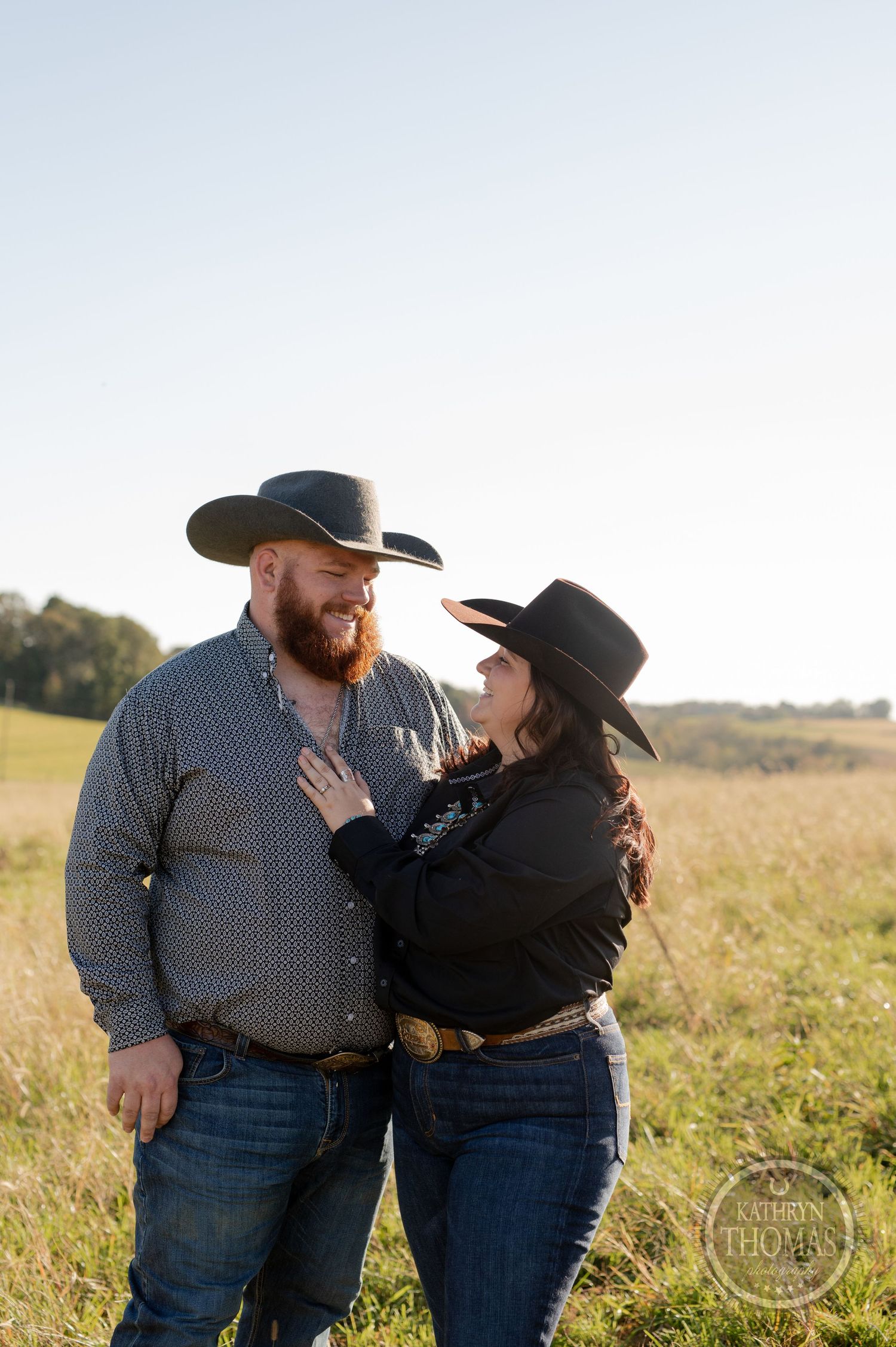 Couple in western attire share intimate moment in sunlit prairie field.