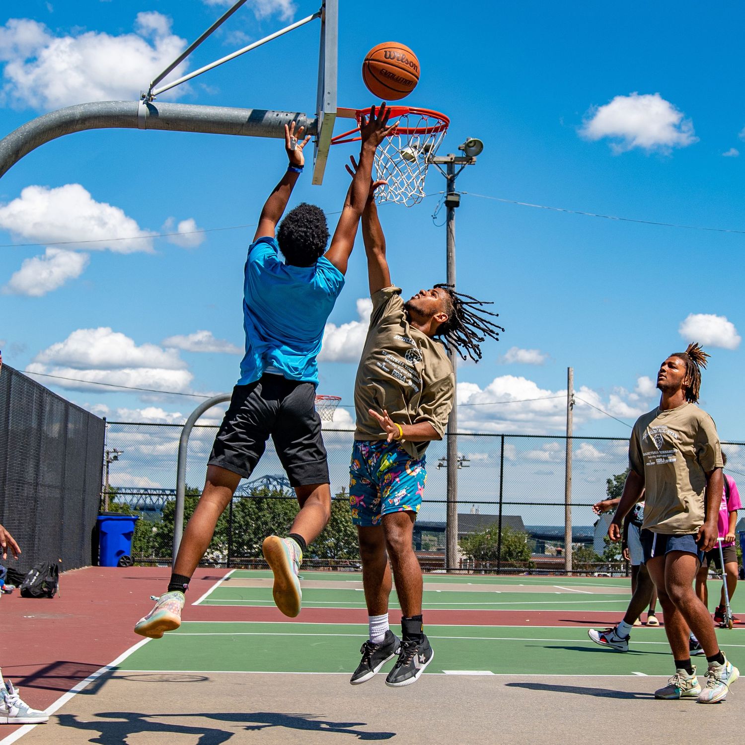 Group of young men playing outdoor basketball on a sunny urban court.