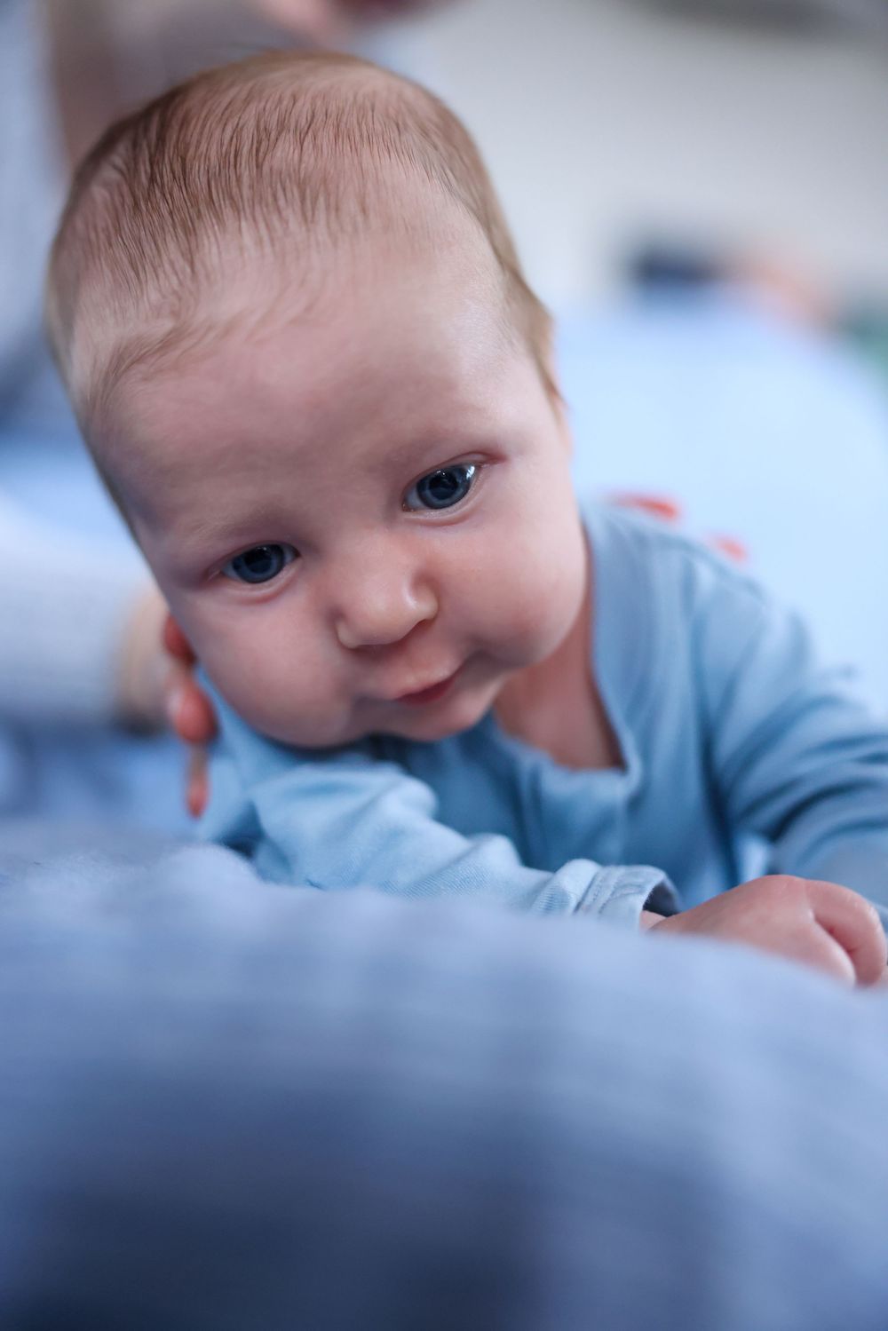 Close-up of alert newborn baby in blue outfit during tummy time.