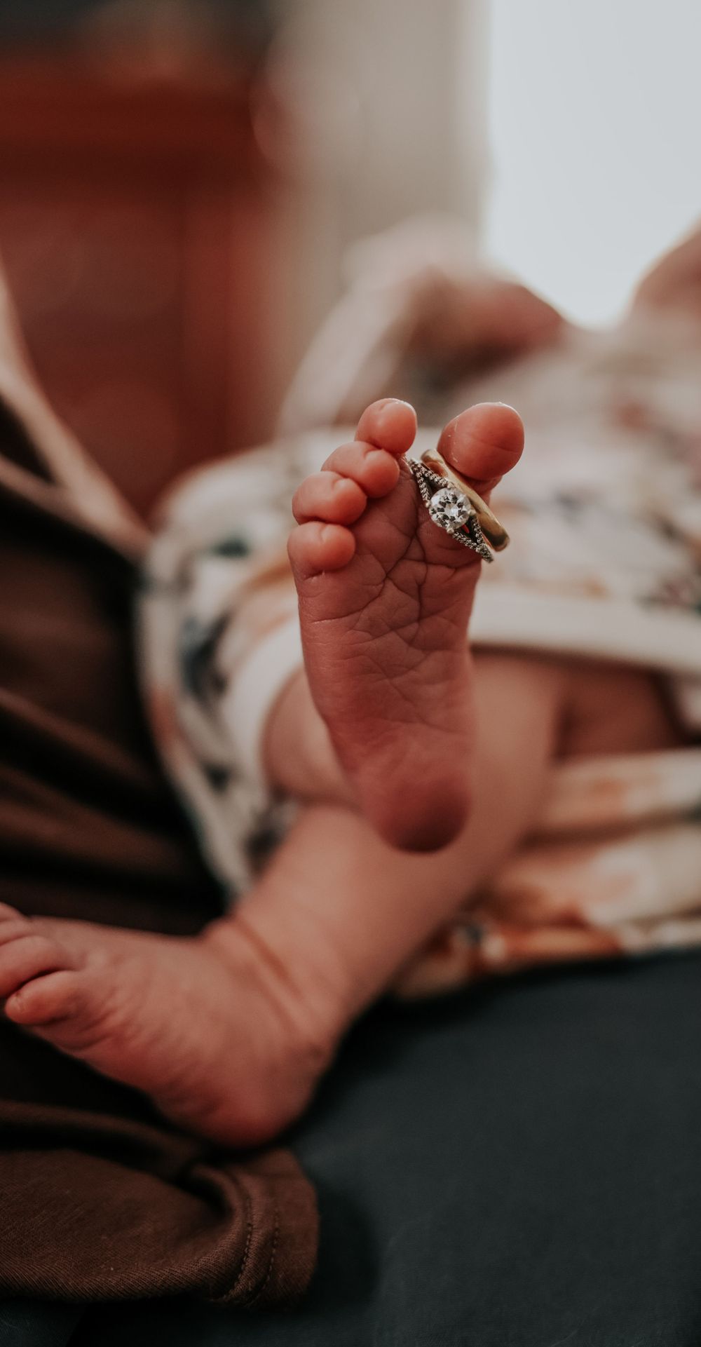 Close-up of newborn baby feet with parents wedding ring balanced on toes.