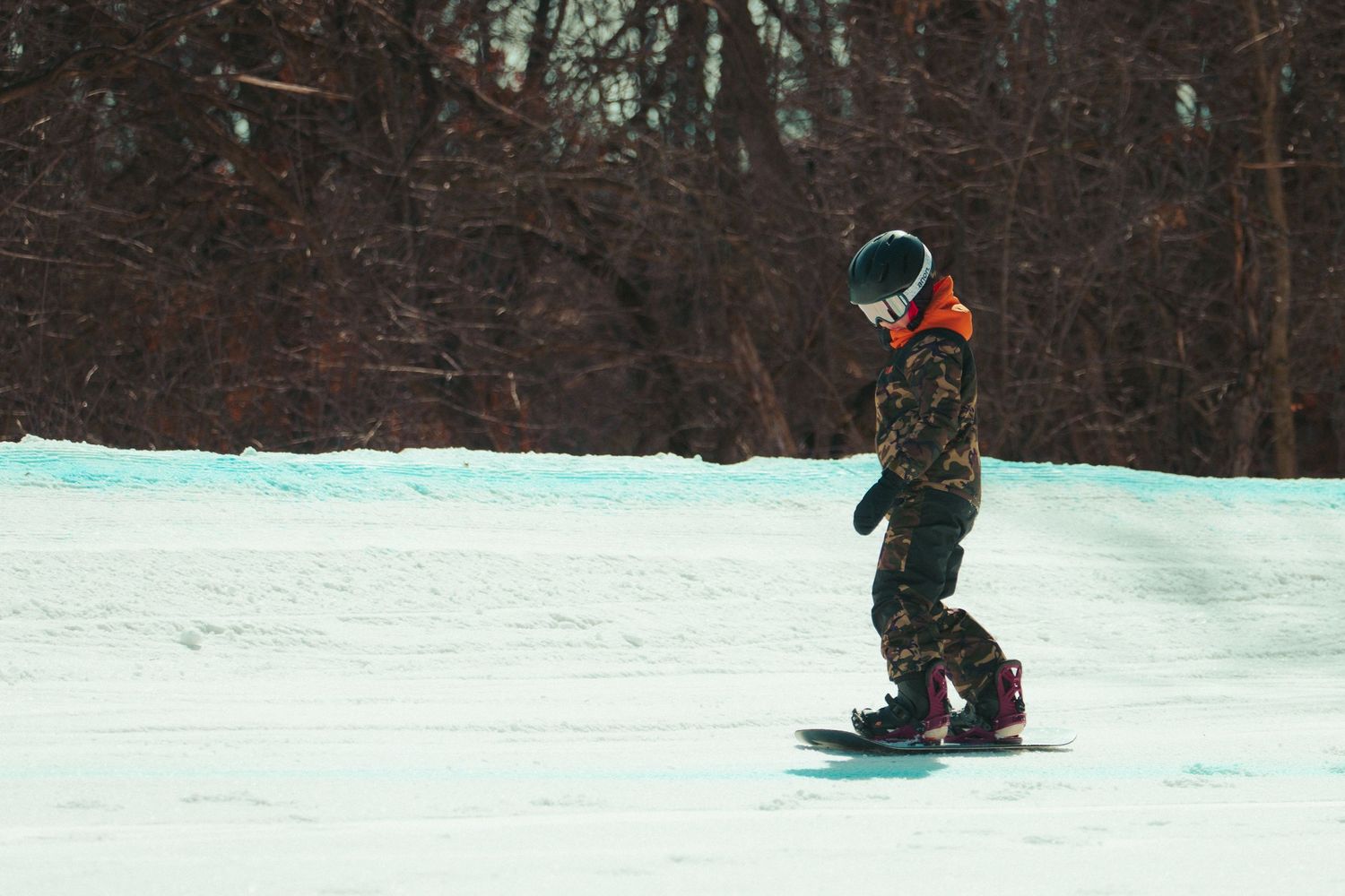 Snowboarder rides down winter slope in camouflage gear.