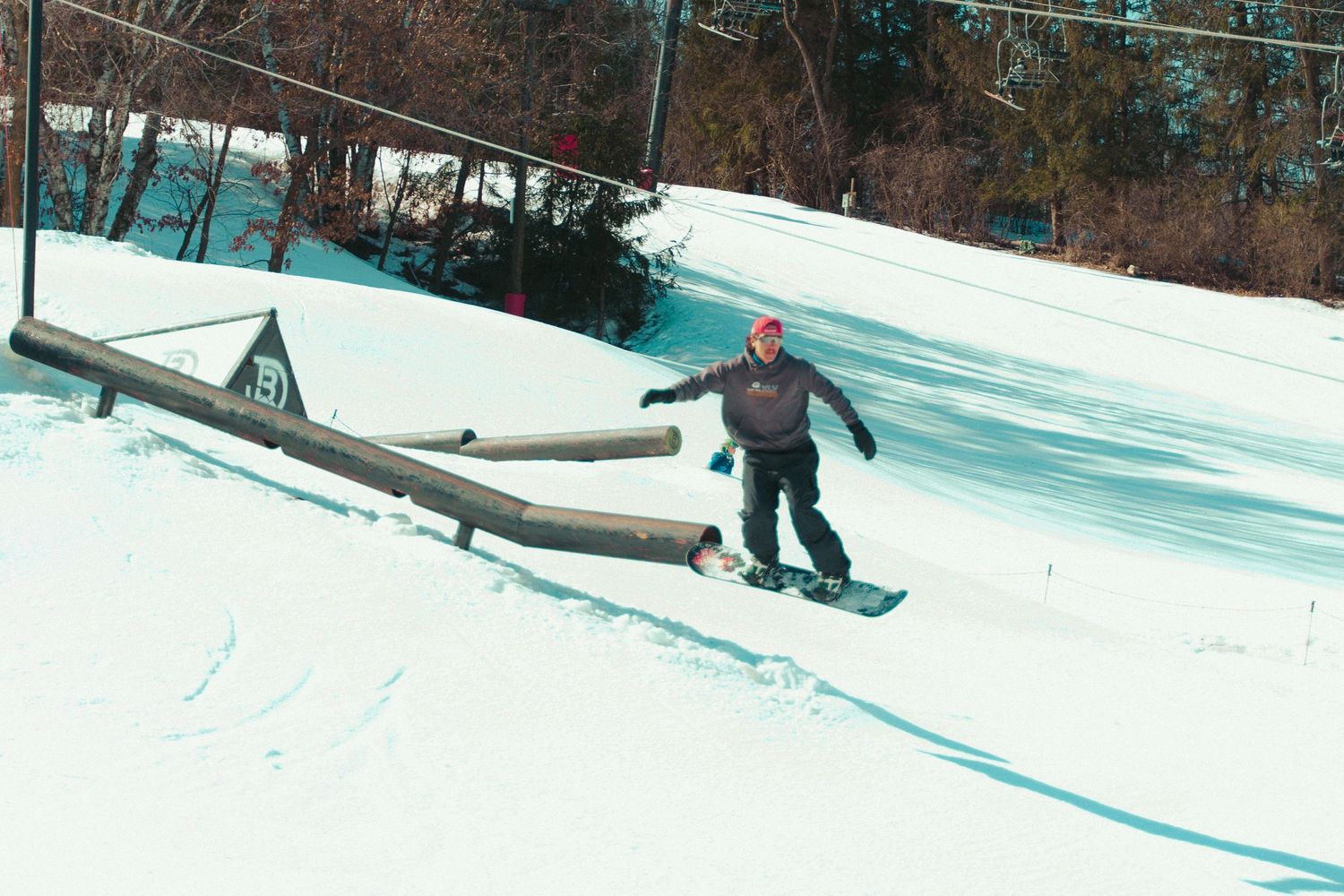 Snowboarder sliding on a rail at a snow terrain park.