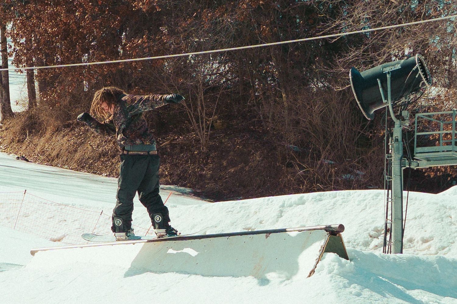 Snowboarder riding past a ski lift pole in winter terrain.