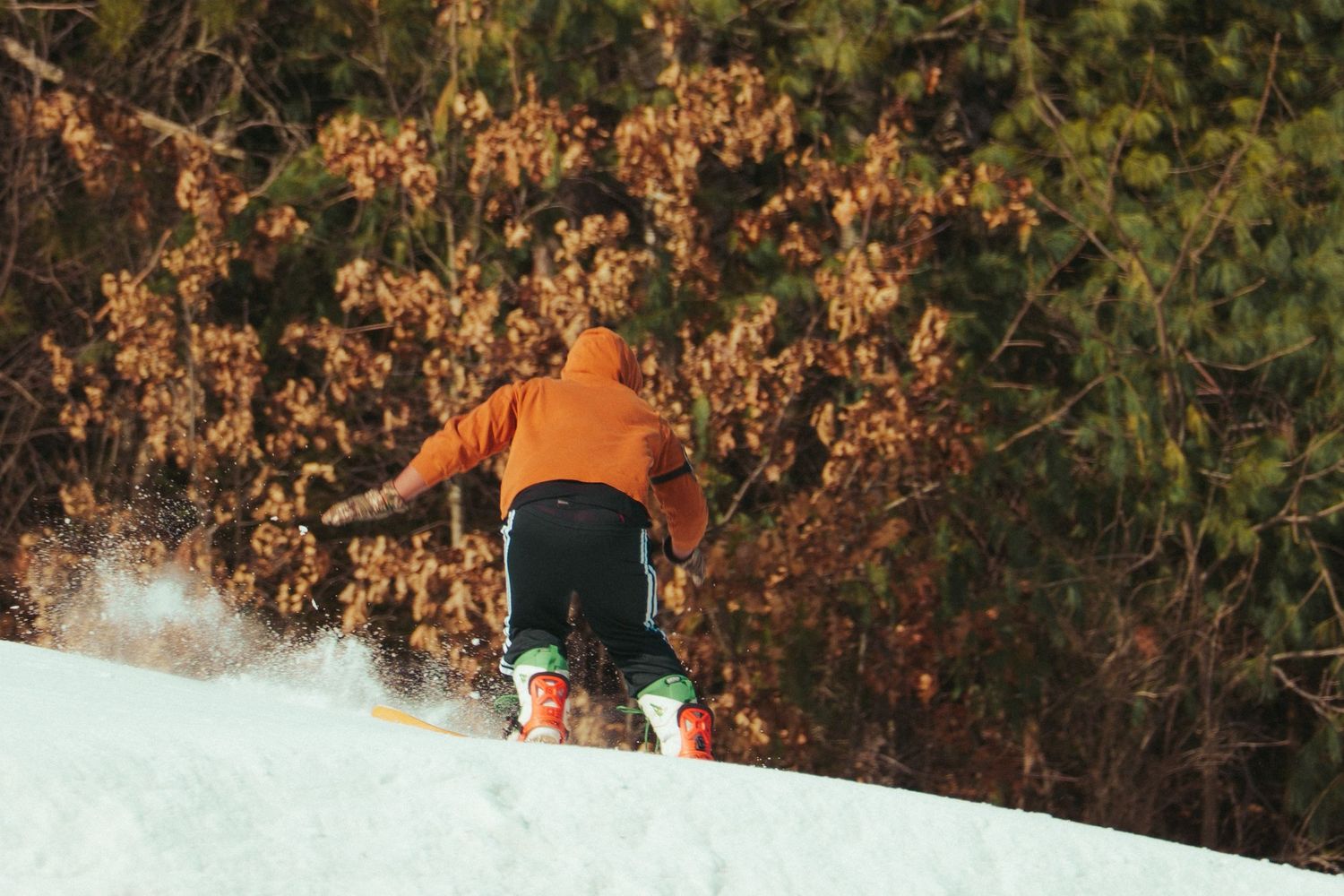 Snowboarder in orange jacket glides down snowy slope at sunset.