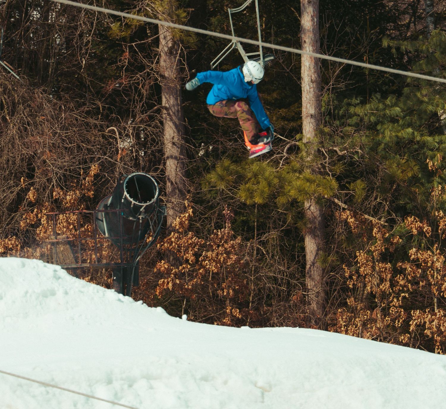 Snowboarder performs aerial jump over snowy terrain against winter forest backdrop.