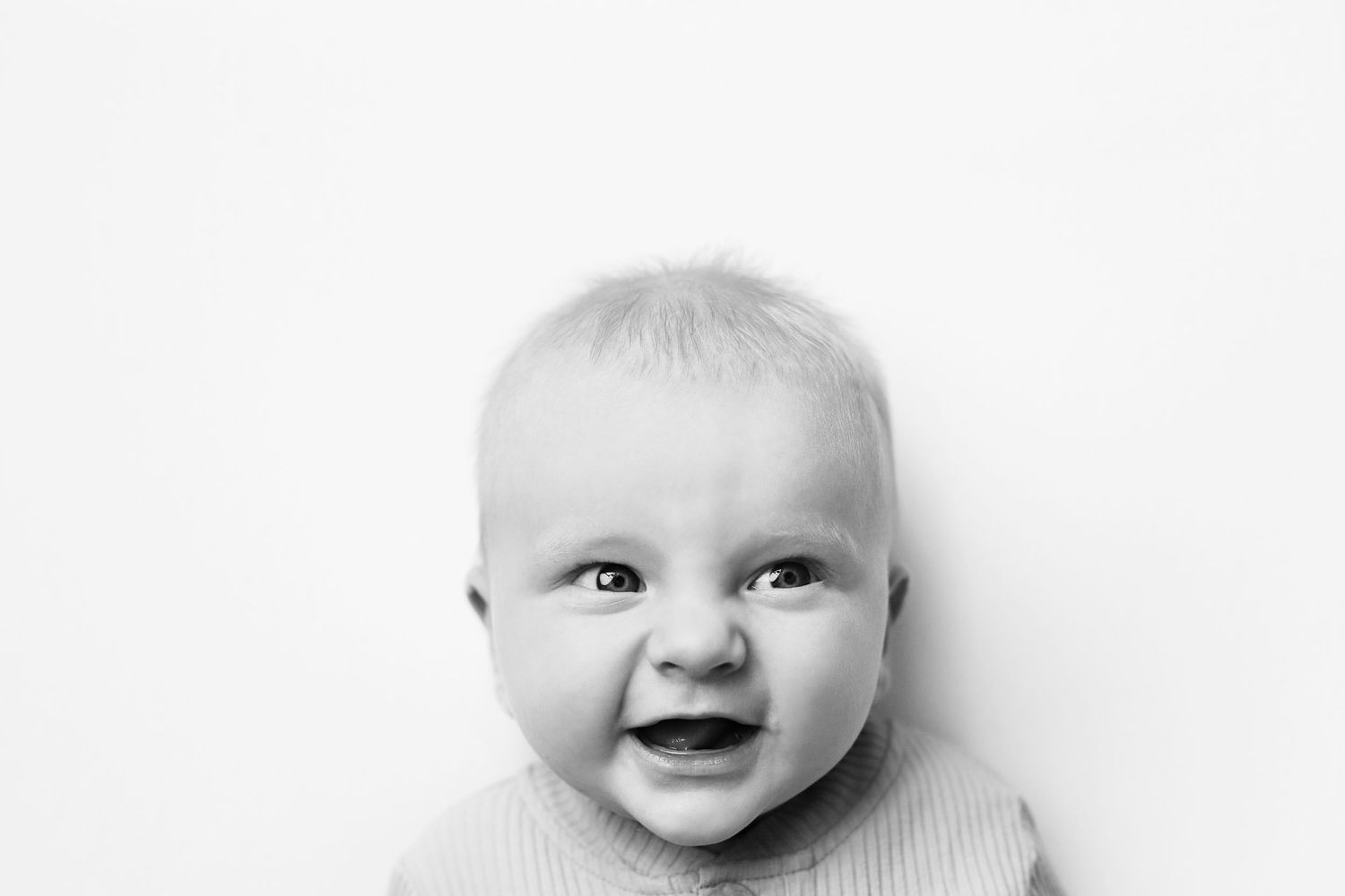 Baby wearing backwards baseball cap and hooded sweatshirt smiles in black and white portrait.