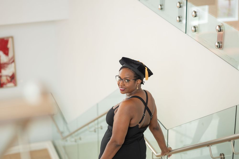 A dancer in black workout attire stretches and practices at a ballet barre in a bright studio space.
