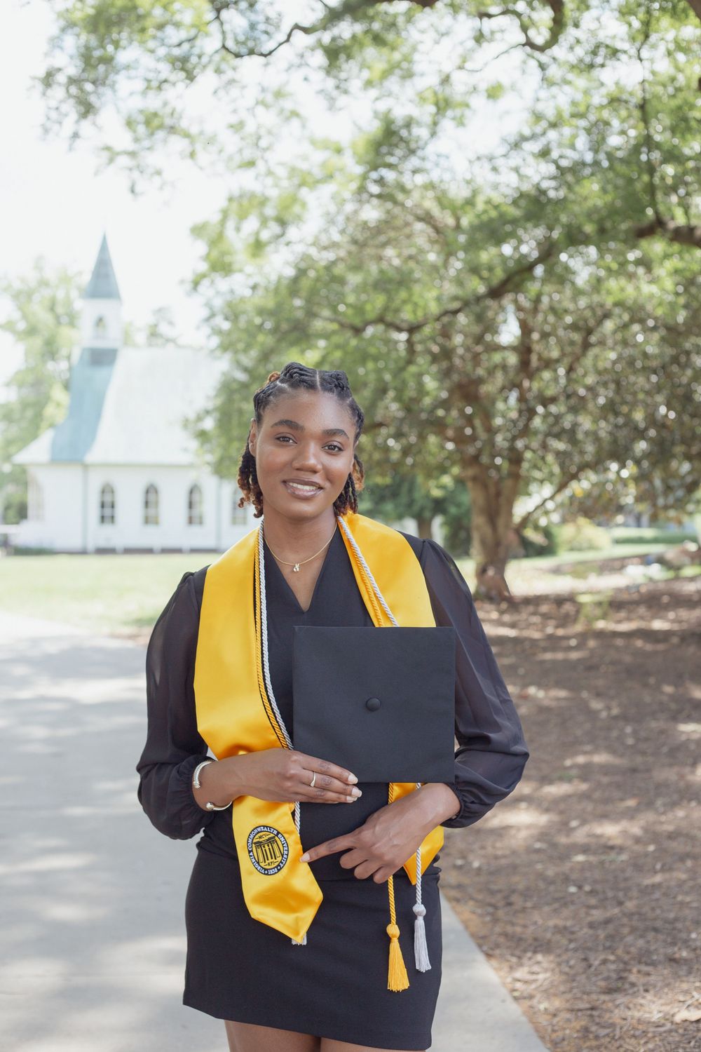 Graduate in cap and gown stands proudly in front of white church.