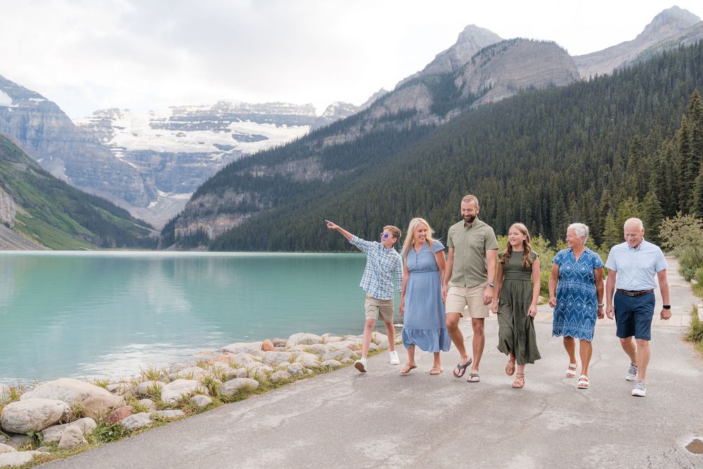 Group of six people walking and smiling along Lake Louise shoreline with turquoise water and Rocky Mountains backdrop.