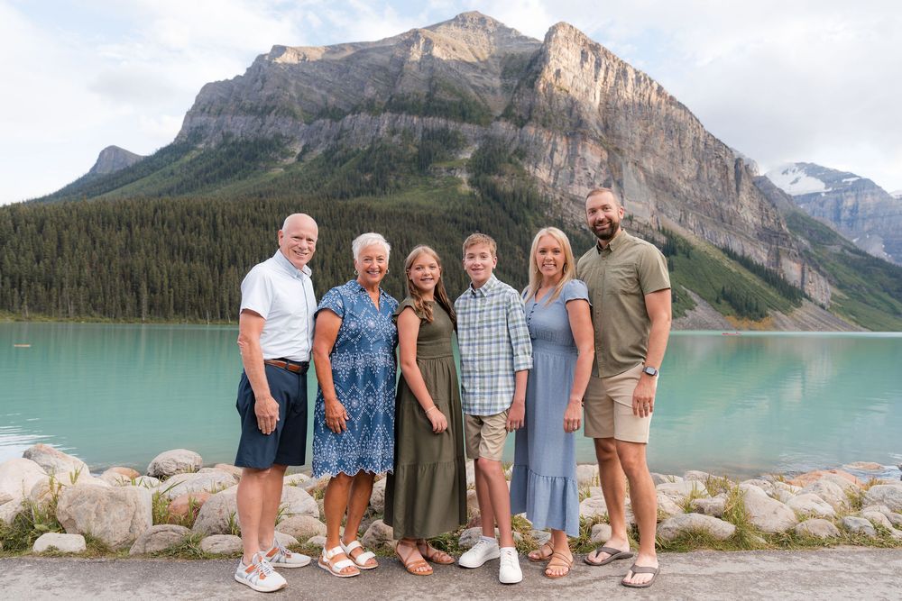 Family of six posing together at Lake Louise with turquoise water and Rocky Mountains in the background.