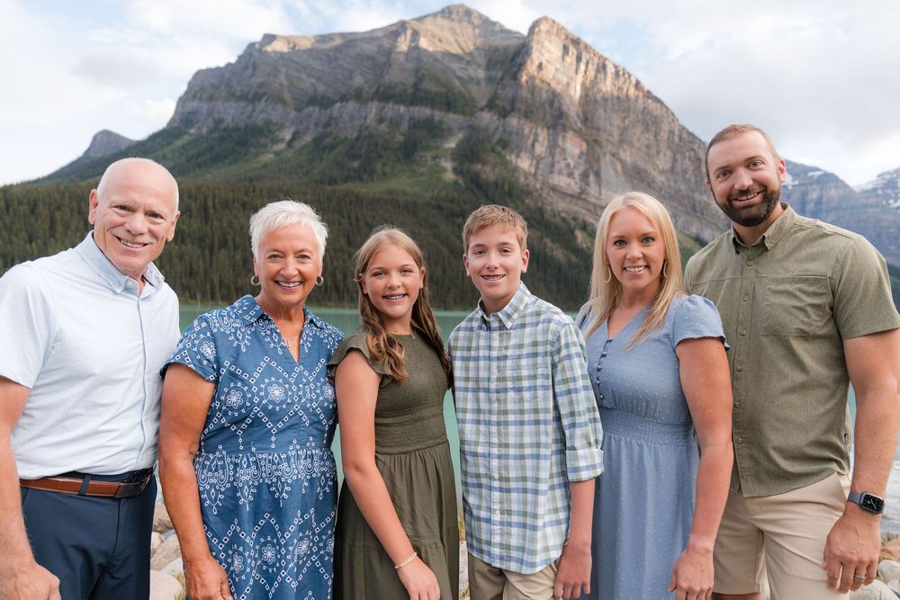 Family of six smiling together with stunning Rocky Mountain peaks in the background.