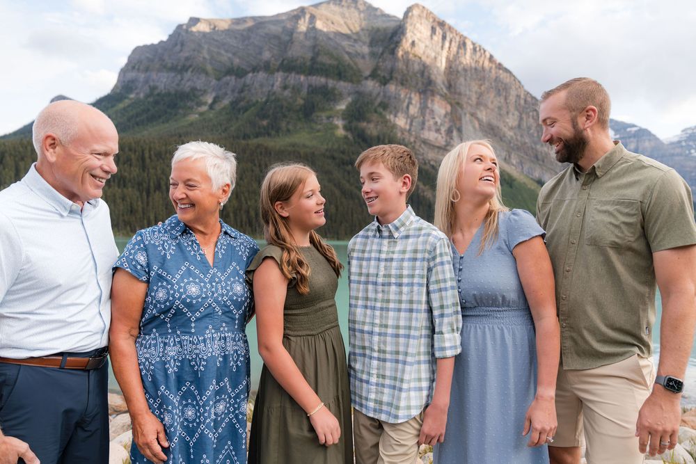Six family members laughing together outdoors with majestic mountain scenery behind them.