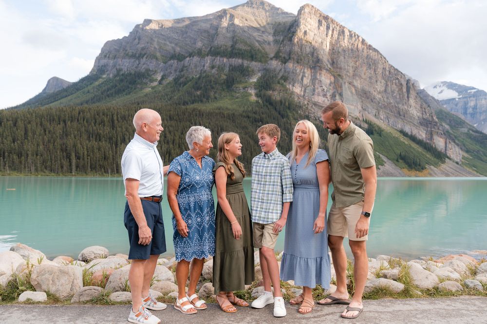 Family of six posing together at turquoise Lake Louise with dramatic Rocky Mountain peaks in the background.