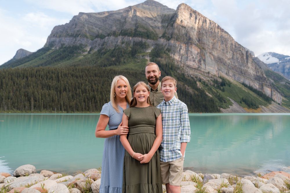 Family of four posing at turquoise Lake Louise with Rocky Mountain backdrop in Banff National Park.