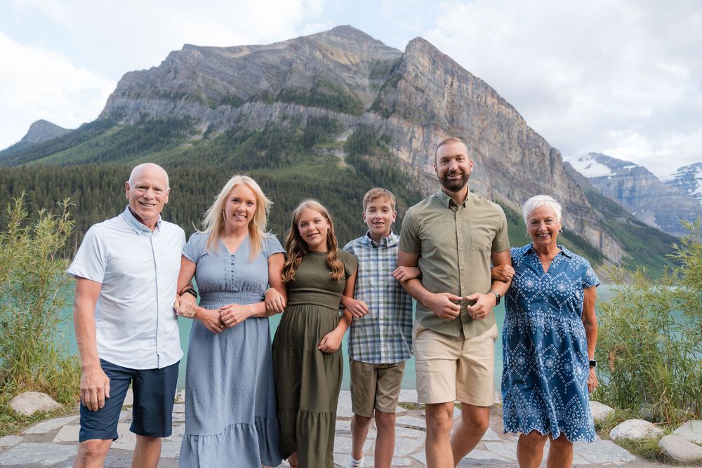 Family of six smiling together with stunning mountain backdrop at Lake Louise, Banff National Park.