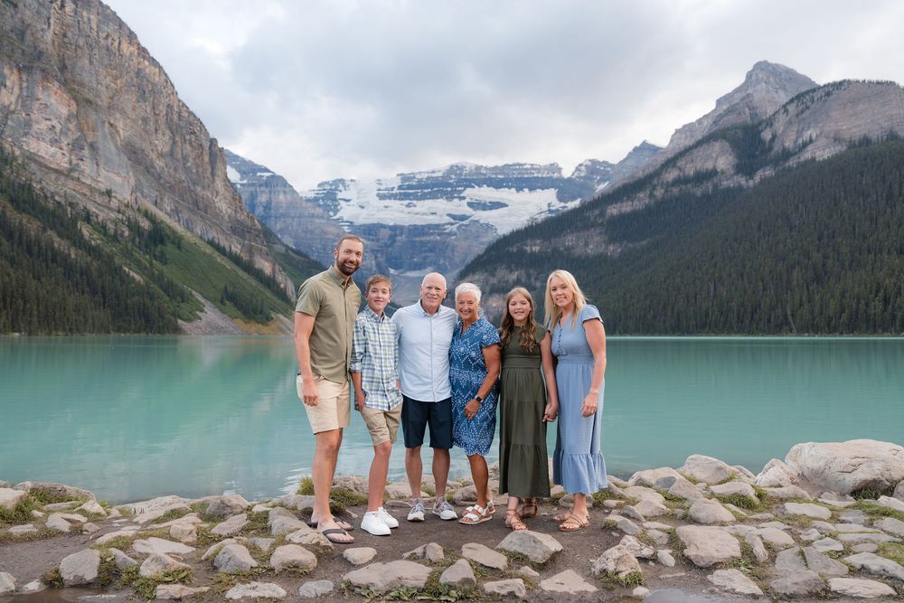 Family of six posing at turquoise Lake Louise with snow-capped Rocky Mountains in Banff National Park, Canada.