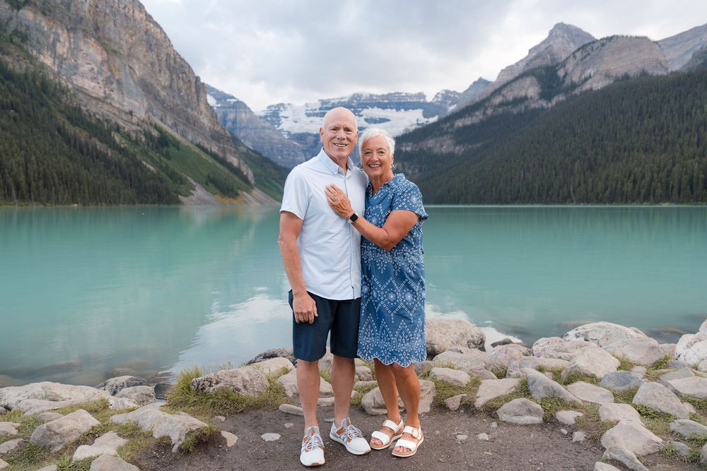 Smiling couple posing at Lake Louise with turquoise water and snow-capped mountains in Banff, Canada.