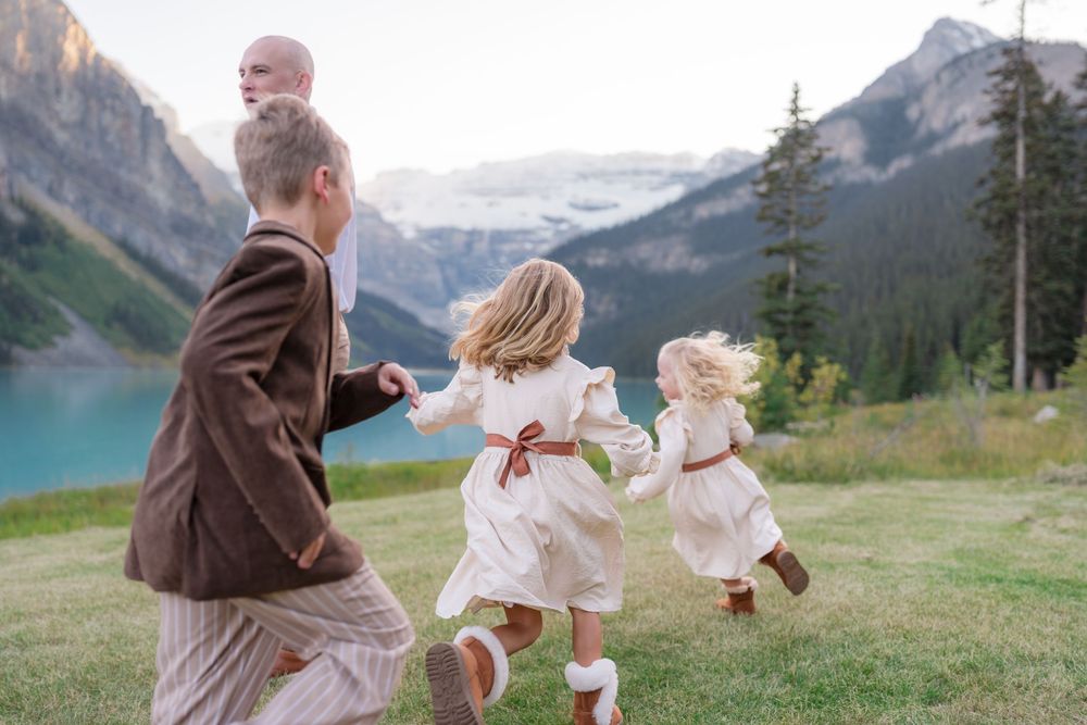 Family running toward turquoise Lake Louise with mountain glacier backdrop during outdoor wedding celebration.