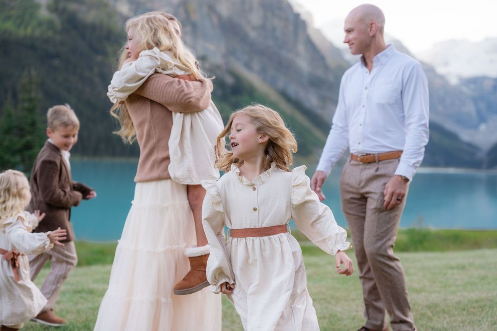 Family enjoying outdoor time near a mountain lake, with children playing and parents smiling in coordinated neutral outfits.