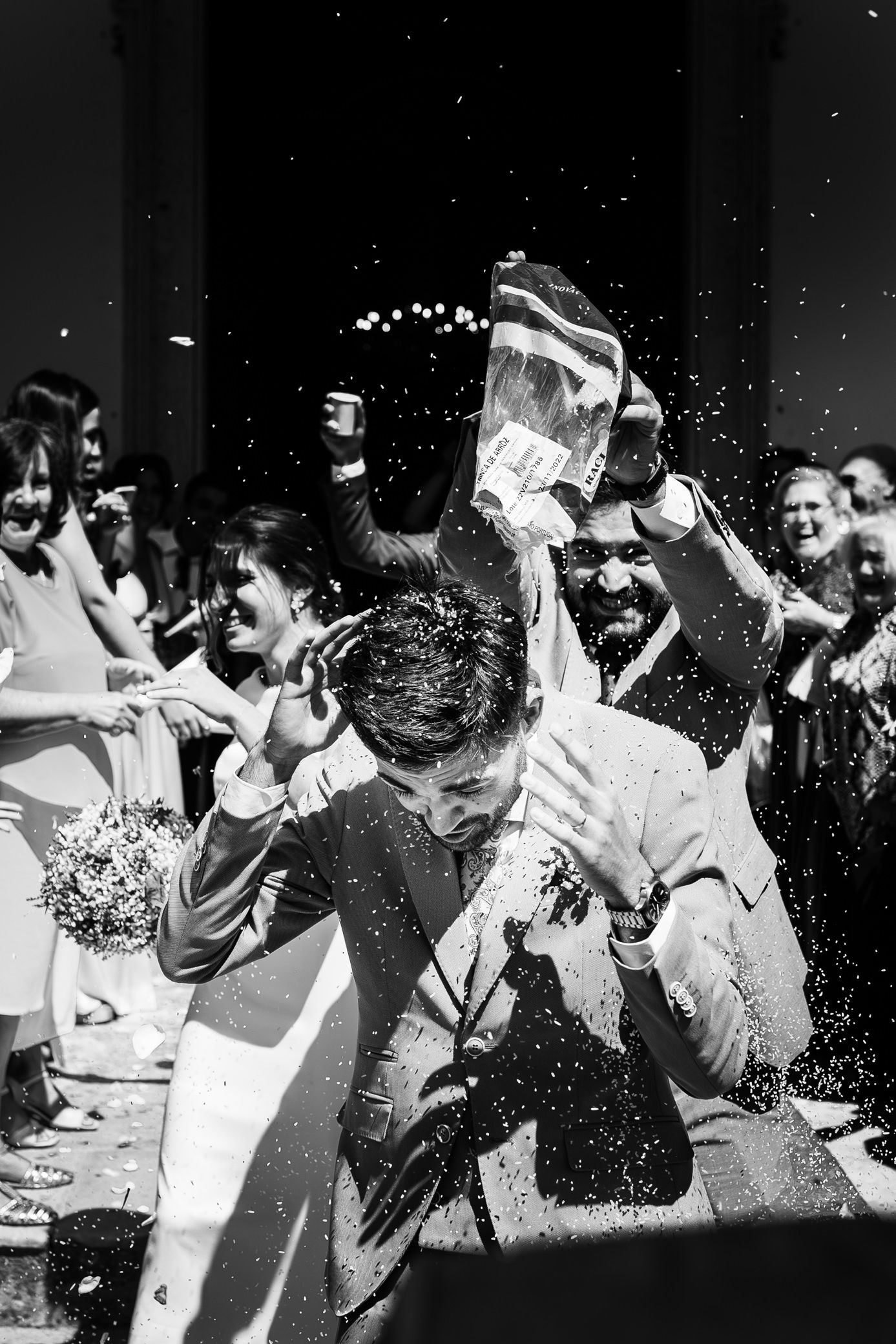 A black and white photograph captures guests joyfully throwing water at a wedding celebration with people laughing and cheering.